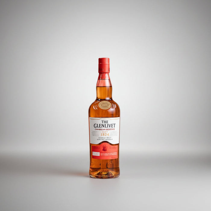 A bottle of The Glenlivet 1824 Single Malt Scotch Whisky stands on a small red pedestal against a plain white background, with decorative dried grass and a small white flower arrangement placed around it.