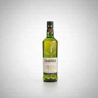 A bottle of Glenfiddich Scotch whisky centered between two clear rocks glasses containing the golden whisky, on a light gray background.